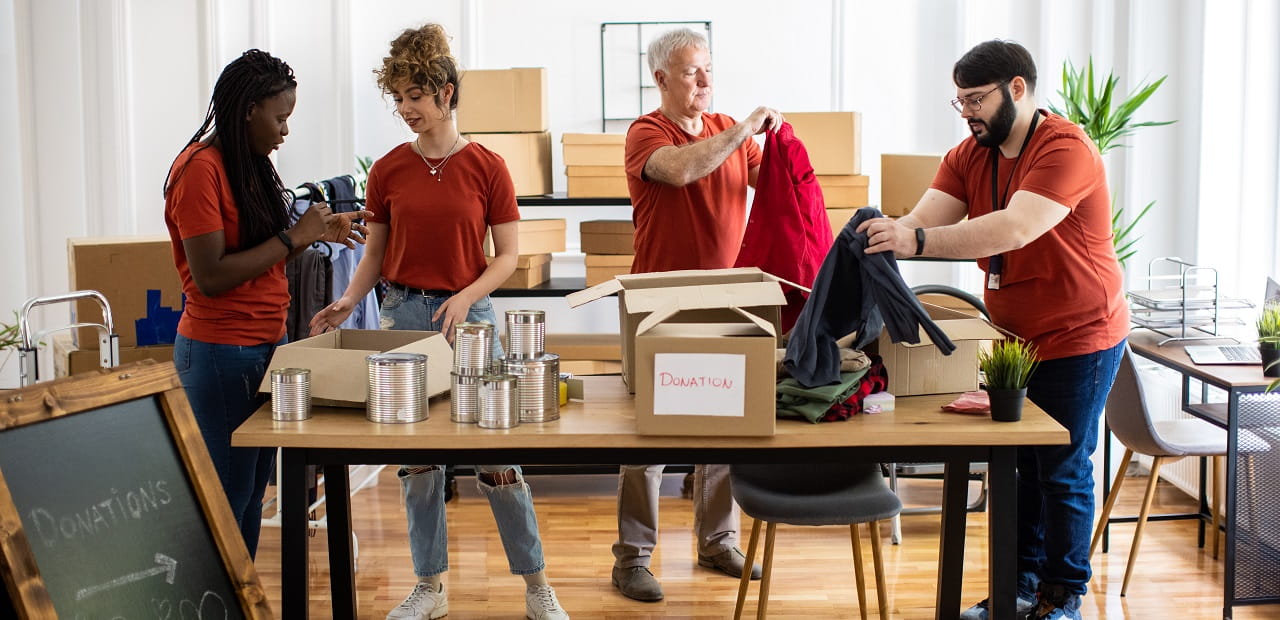 Group of four employees packs household items in boxes. 