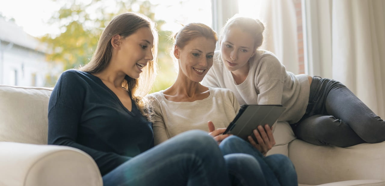 Mother and two daughters looking at tablet on a couch.