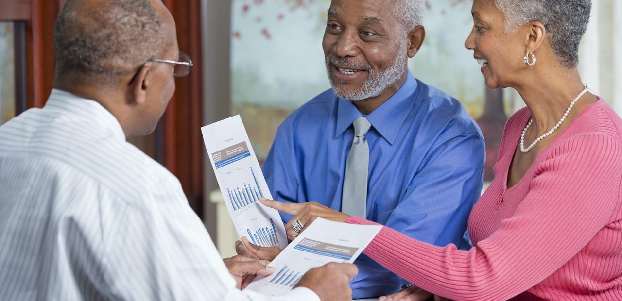 Couple meets with a financial advisor while they examine charts on sheets of paper. 