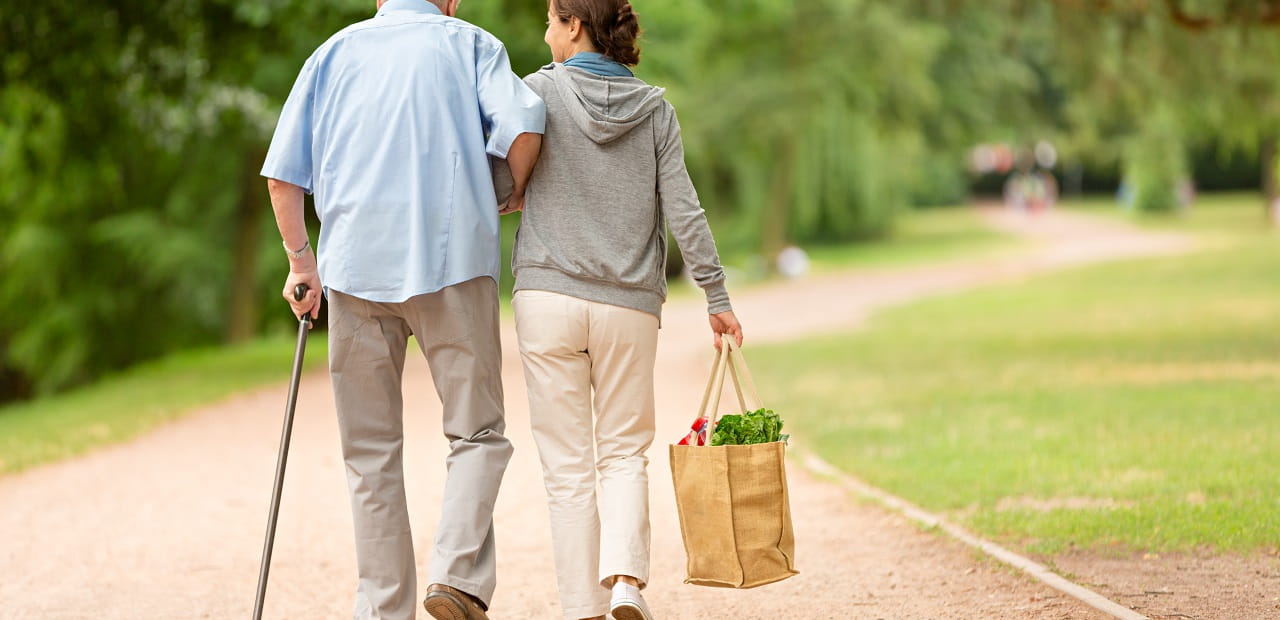 Elderly man and younger woman walk together through a park. 