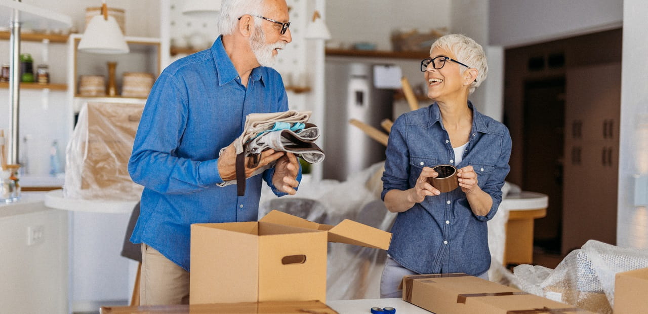 Senior couple packs for a move while smiling at each other. 